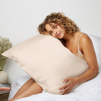 Woman looking happy getting out of bed while hugging a pillow in Dore and Rose Silk Pillowcase in the color Champagne Beige