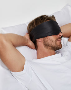 Man looking relaxed lying on a bed while wearing Dore and Rose Black Silk Sleeping Eyemask