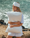 Woman standing comfortably outdoors wearing a blue and white stripes Silk Sleeping Mask and hugging a blue and white stripes silk pillowcase