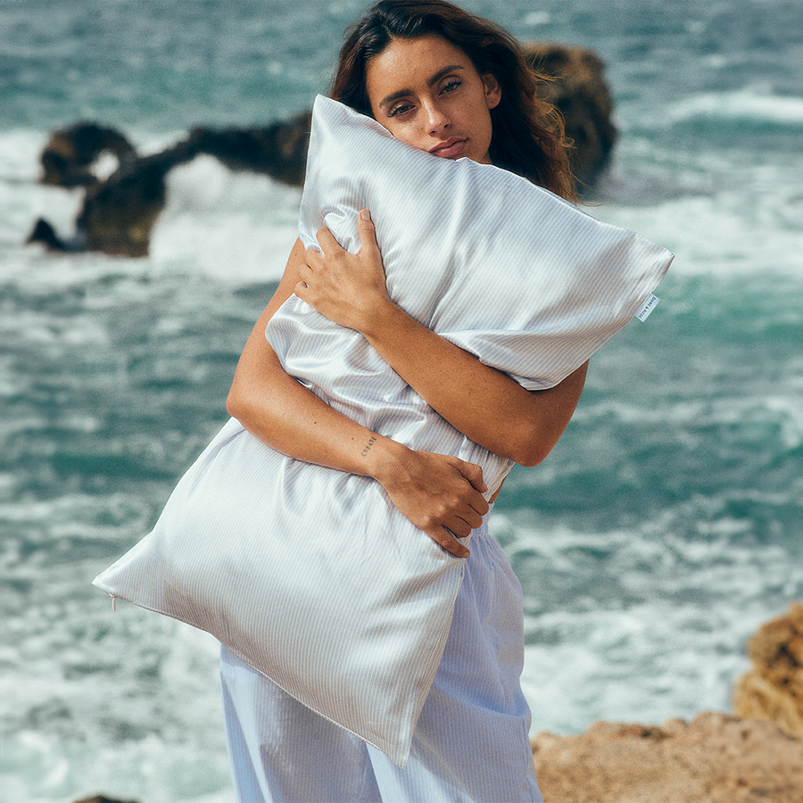 Woman standing comfortably hugging a pillow with the Dore and Rose Silk Pillowcase in the color Blue and White stripes