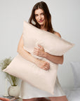 Woman looking happy while on her knees in bed hugging a pillow in Dore and Rose Silk Pillowcase in the color Champagne Beige