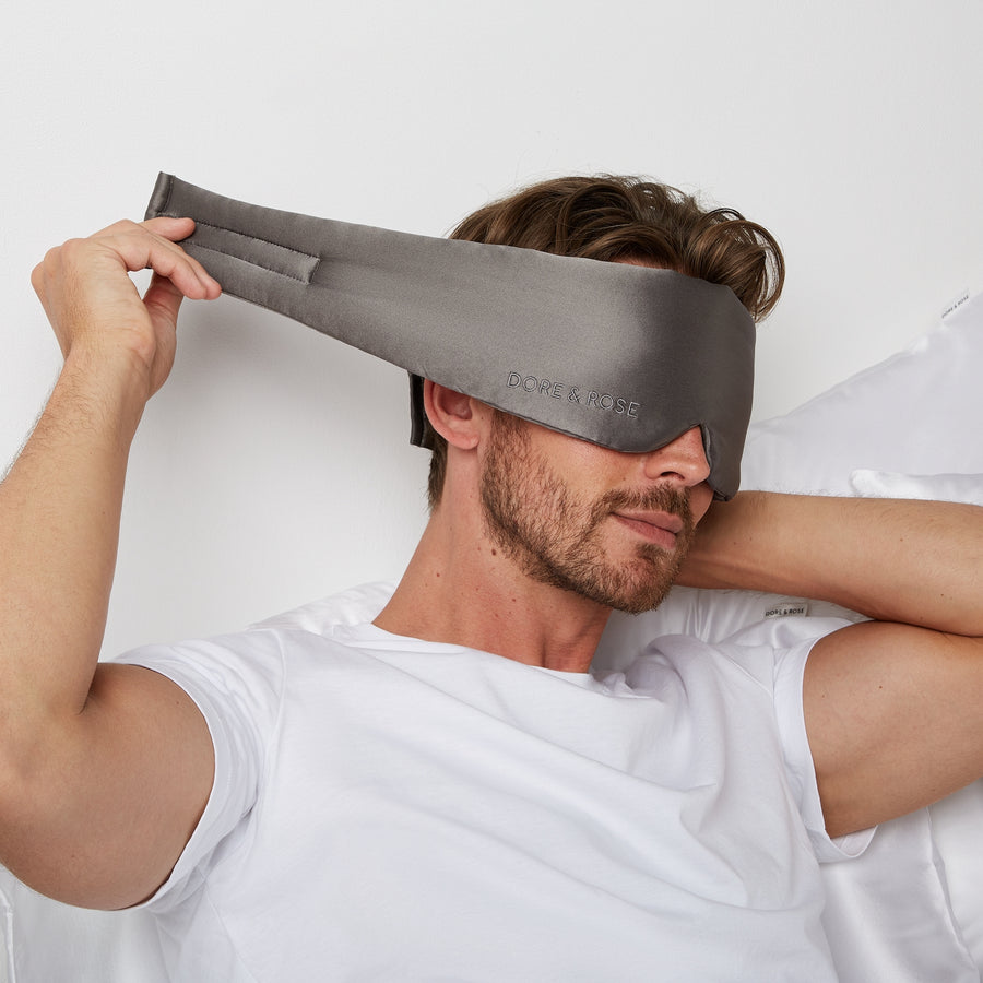 Man getting ready for bed by wearing a Luxury Soft Silk Sleeping Eye Mask from Dore and Rose in the color Gray