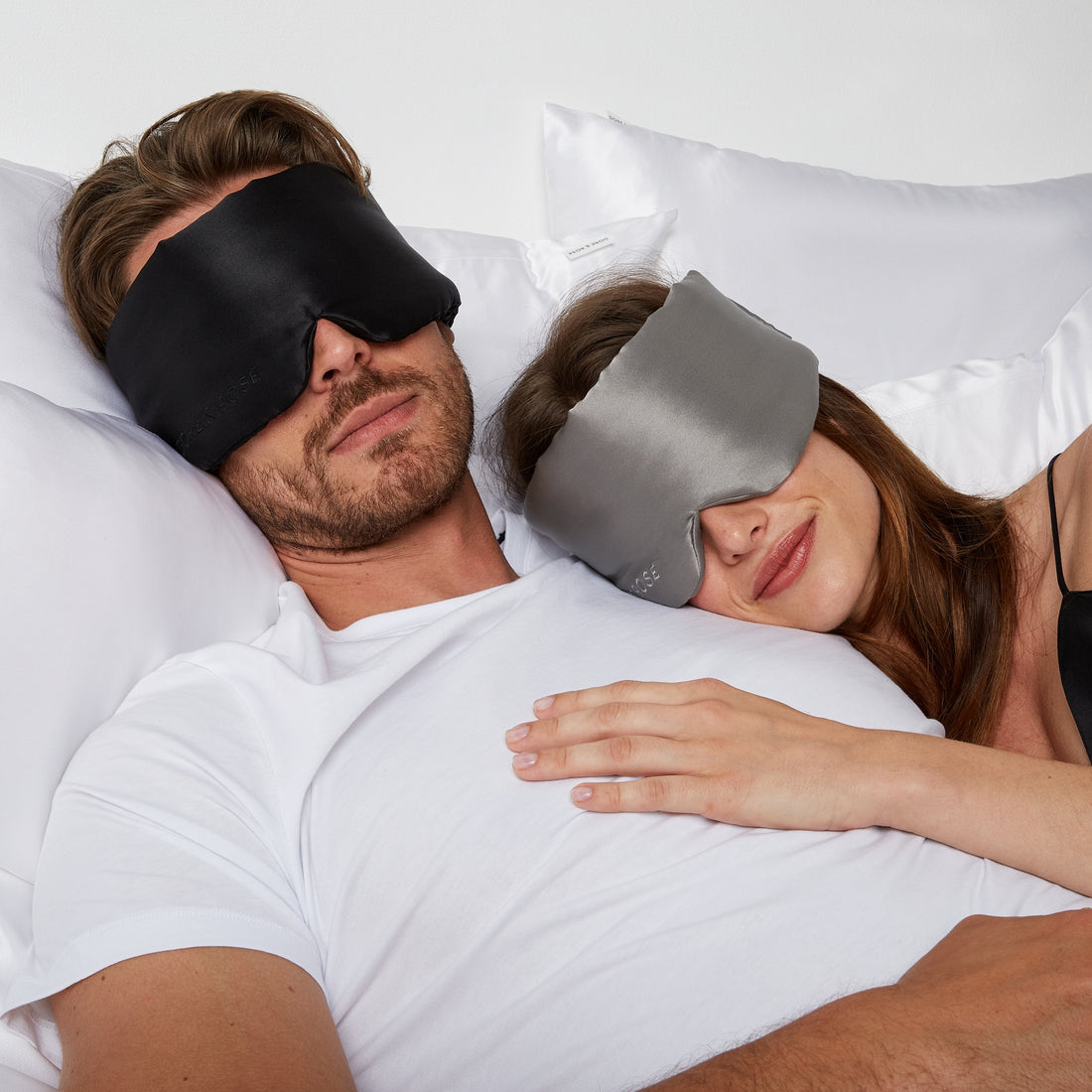 Couple lying comfortably in bed wearing a Silk Sleeping Eyemask from Dore and Rose in the colors Gray for the woman and Black for the Man