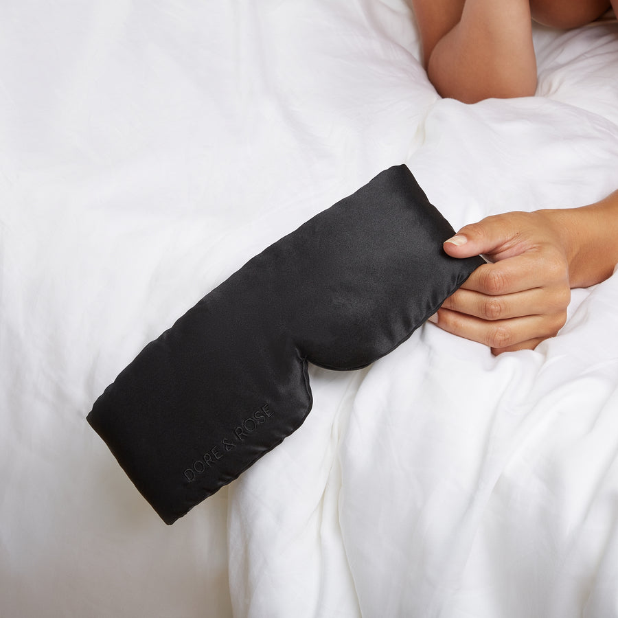 Woman's hand holding a Silk Sleeping Eyemask from Dore and Rose in the color Black