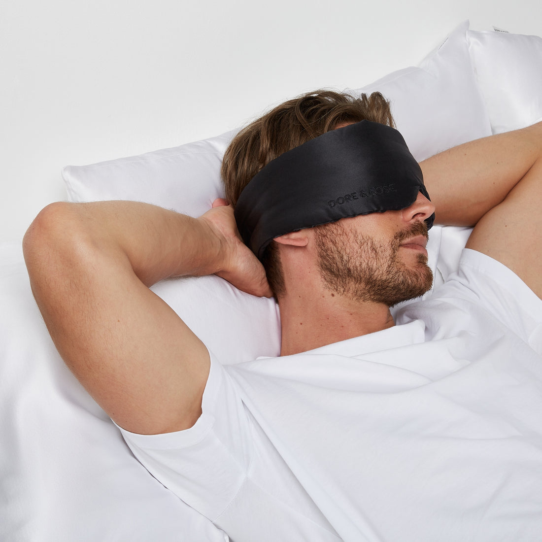 Man looking relaxed lying on a bed while wearing Dore and Rose Black Silk Sleeping Eyemask