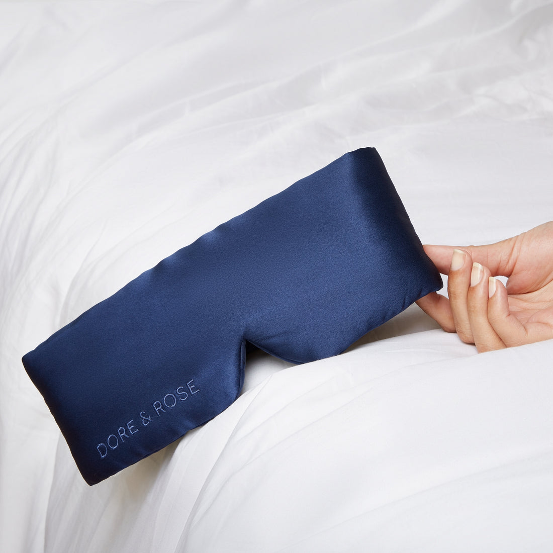 Woman's hand holding a Silk Sleeping Eyemask from Dore and Rose in the color Navy Blue