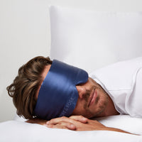 Man lying comfortably in bed wearing a Silk Sleeping Eyemask from Dore and Rose in the color Navy Blue
