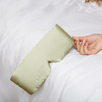 Woman's hand holding a Silk Sleeping Eyemask from Dore and Rose in the color Olive Green