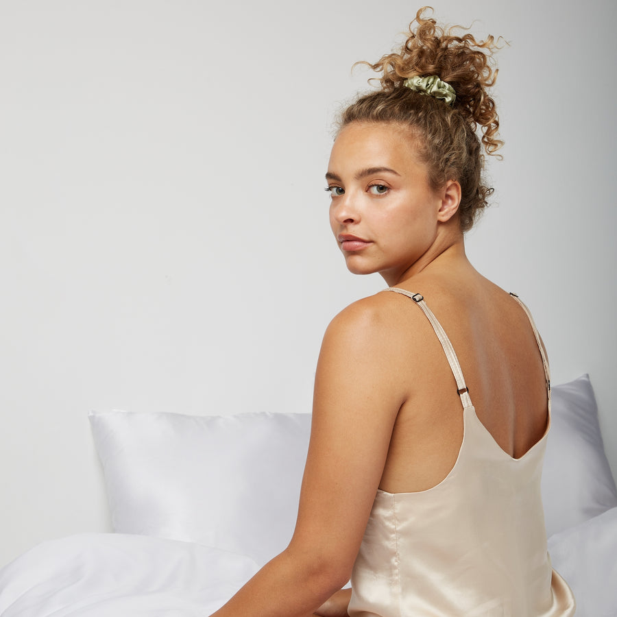 Woman sitting in bed waking up wearing a silk scrunchie from Dore and Rose in the color Olive Green