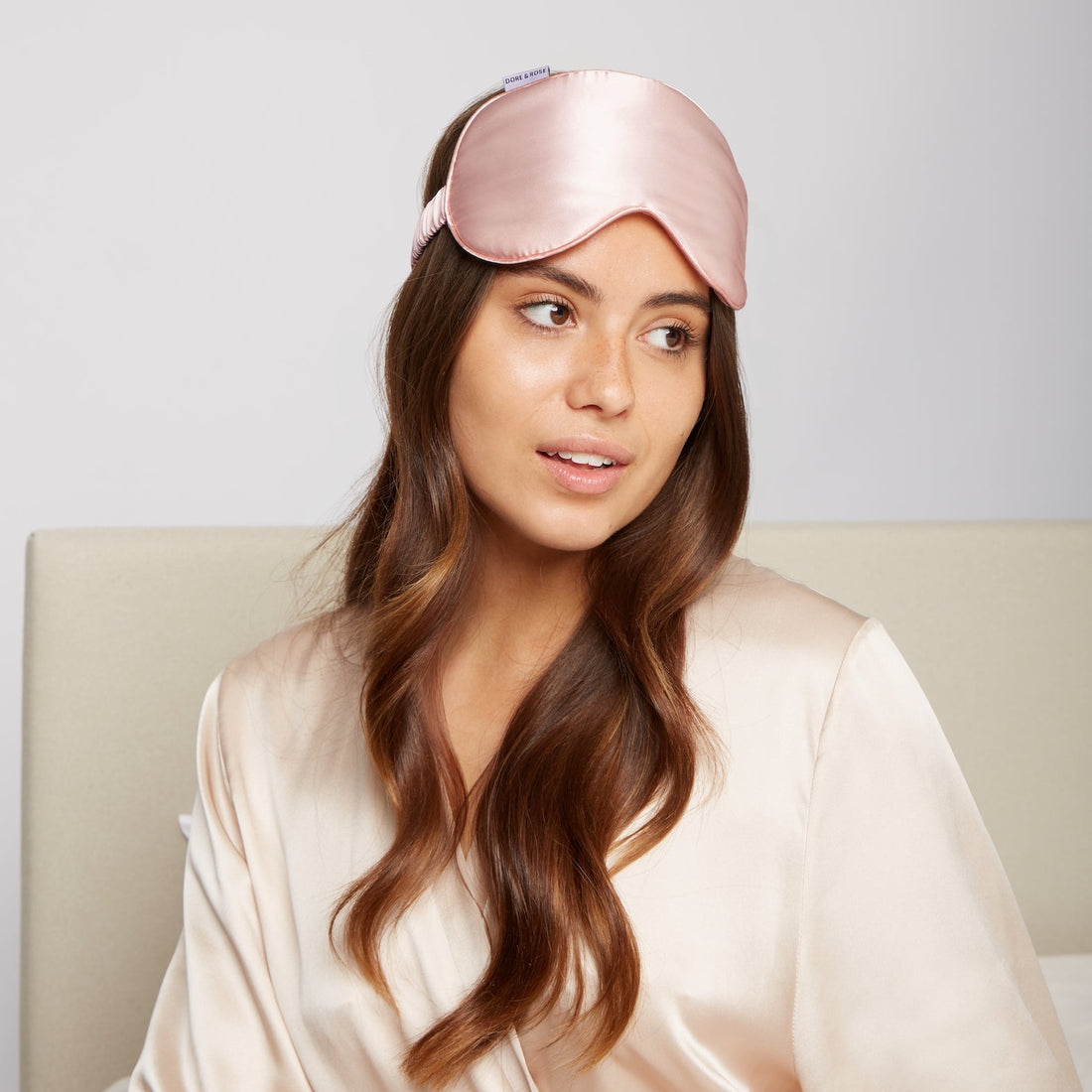 Woman waking up in the morning wearing the Premium Stretchable Silk Sleep Eye Mask from Dore & Rose in the color Pink